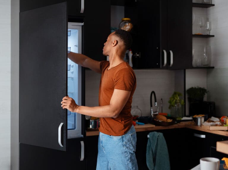 Synthesis Peptides - A person wearing a brown t-shirt and jeans is opening a refrigerator in a modern kitchen, perhaps searching for research peptides among the various kitchen items and food on the counter behind them.